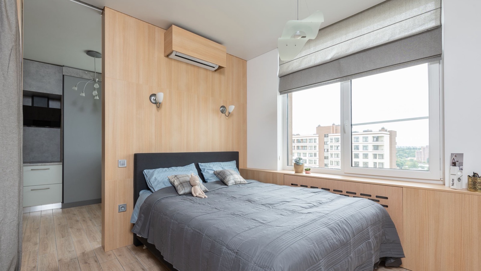 Wall-mounted mini split indoor unit in a wood-clad cover above a bed in a bright bedroom, one of the two rooms a DIY dual zone mini split serves