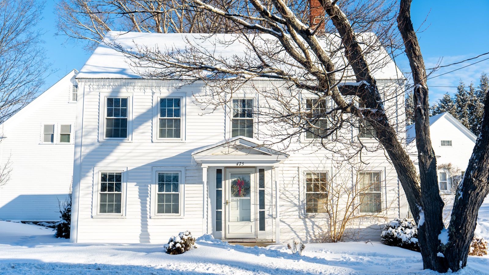 Two-story white house under fresh snow on a sunny winter day, the kind of cold-climate home a MRCOOL Hyper Heat DIY mini split gets sized for